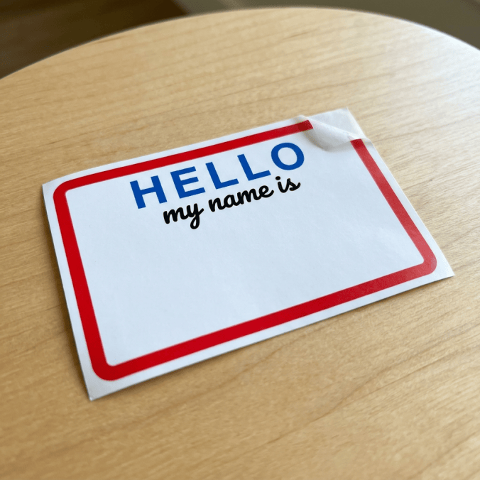Blank name tag reading “HELLO my name is” on a wooden table